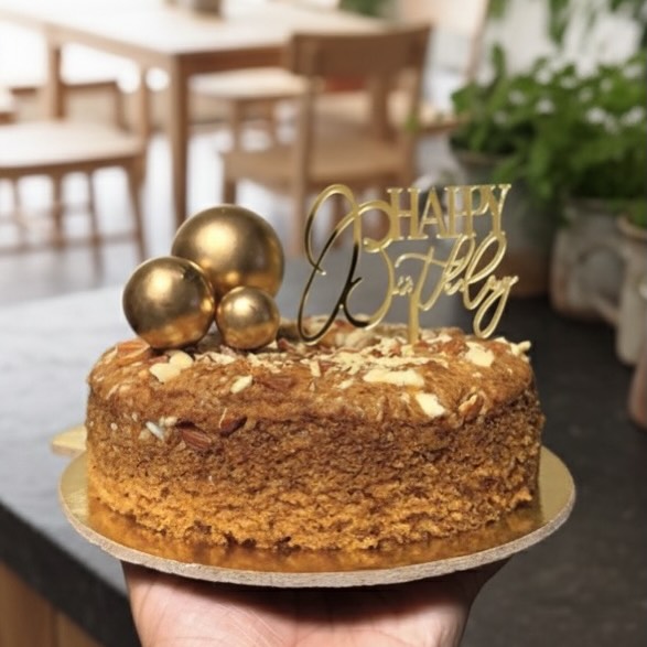 A homemade birthday cake with gold balloons and a Happy Birthday topper